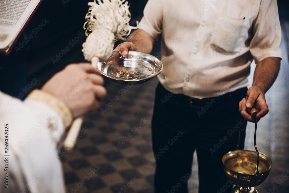 priest blessing golden wedding rings on plate in church before wedding ceremony, religion traditions.