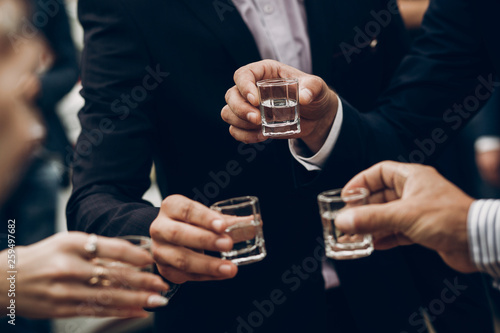 people toasting holding glasses of vodka cheering at wedding reception, celebration outdoors, catering in restaurant. christmas and new year