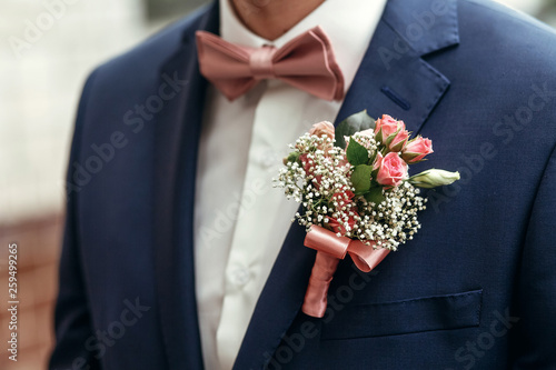 stylish groom or groomsmen in suit with pink roses boutonniere and bow tie posing, getting ready in morning for wedding ceremony. photo