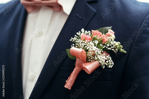 stylish groom or groomsmen in suit with pink roses boutonniere and bow tie posing, getting ready in morning for wedding ceremony. photo