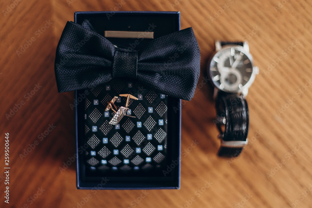 golden cuff links bow tie and watch on wooden table. luxury groom set. wedding preparation in morning. space for text. top view golden cuff links bow tie and watch on wooden table. luxury groom set. wedding preparation in morning. space for text. top view