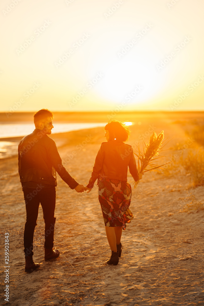 Fototapeta premium Enjoying time together. Stylish and loving couple enjoying each other by the sea. The couple is young and in love. The concept of youth, love and lifestyle. Beautiful sunset on a summer day.