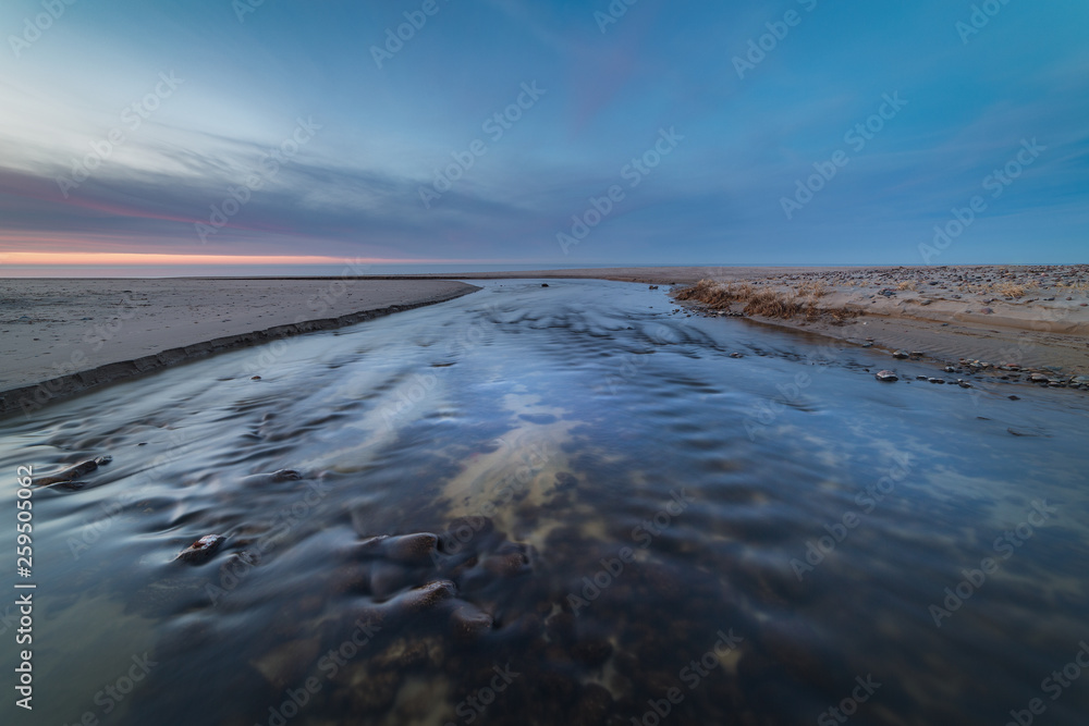 Wide and shallow stream on the shore of the Baltic sea at sunset