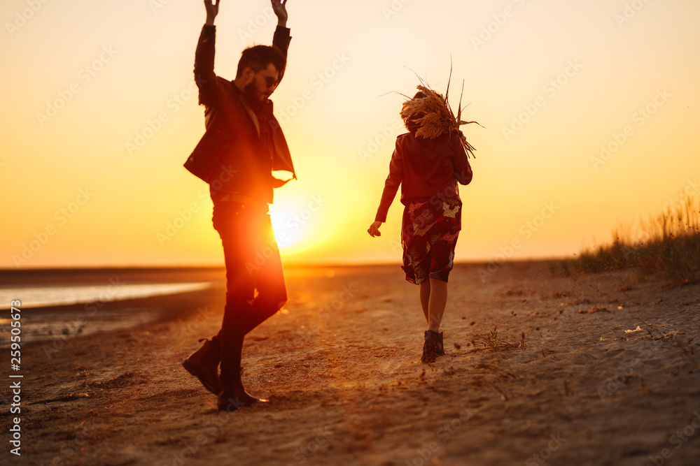 Fototapeta premium Enjoying time together. Stylish and loving couple enjoying each other by the sea. The couple is young and in love. The concept of youth, love and lifestyle. Beautiful sunset on a summer day.