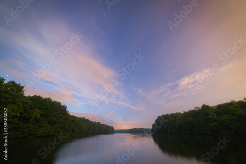 Small calm lake at night. Starry and cloudy sky