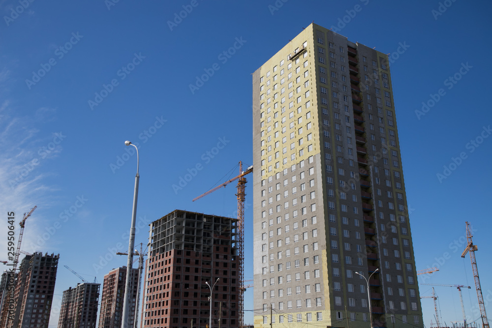 Fototapeta premium Construction of a multi-storey residential complex. Crane near the building under construction. Background construction site.