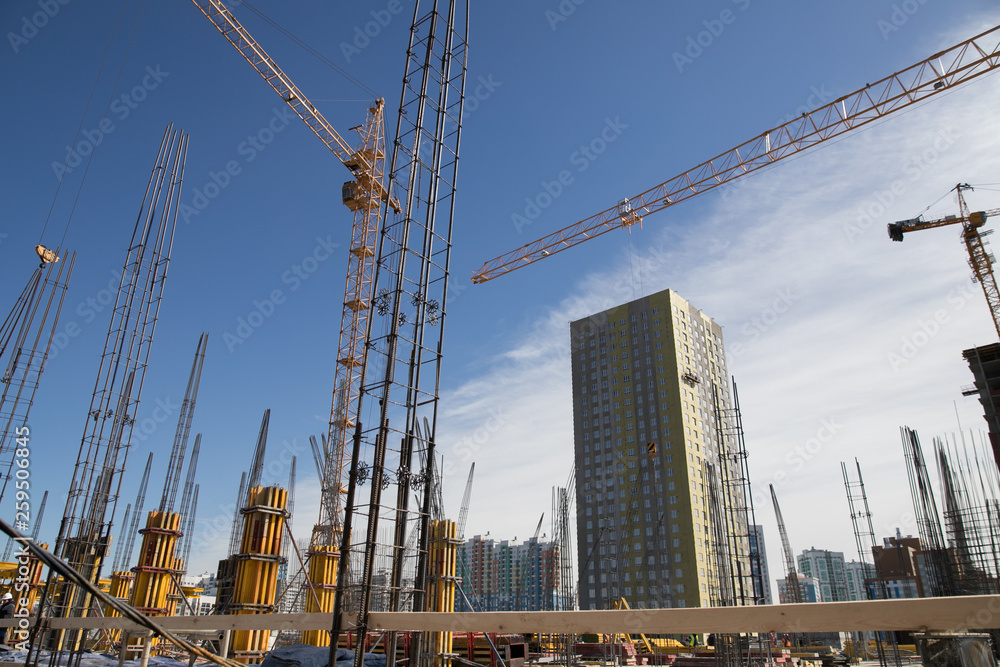 Concrete pillars on construction site. Building of skyscraper with crane, tools and reinforced steel bars.