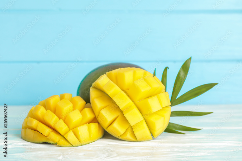 Cut ripe mangoes and palm leaf on white table against color background, space for text