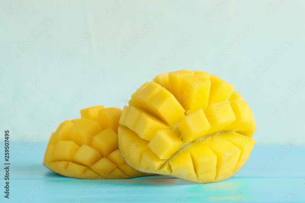 Cut ripe mangoes on color table against white background, closeup