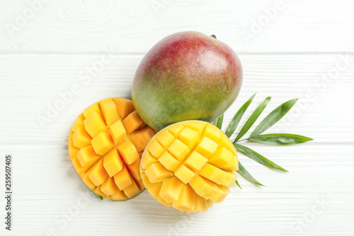 Cut ripe mangoes and palm leaf on white background, space for text