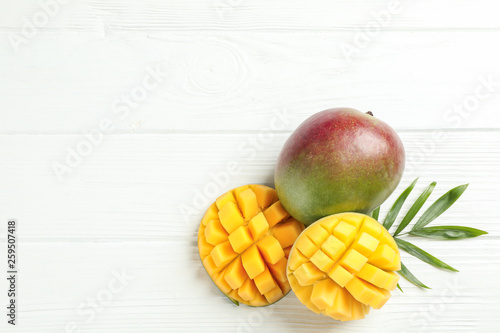 Cut ripe mangoes and palm leaf on white background, space for text