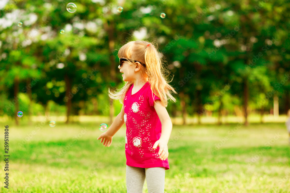 Happy little blond girl blows soap bubbles in summer park Happy little blond girl blows soap bubbles in summer park
