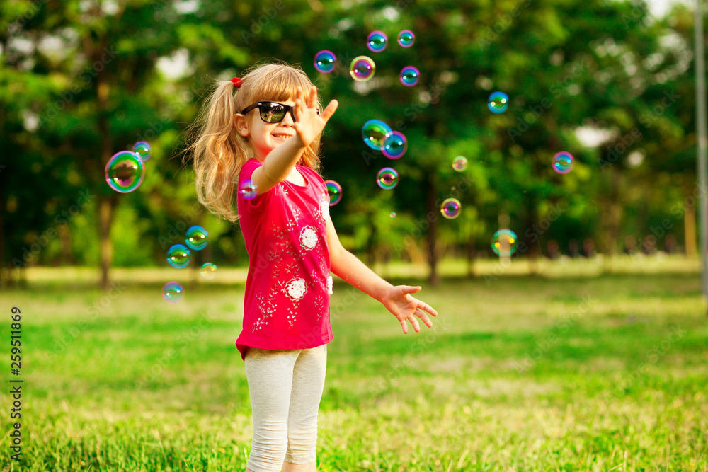 Happy little blond girl blows soap bubbles in summer park Happy little blond girl blows soap bubbles in summer park