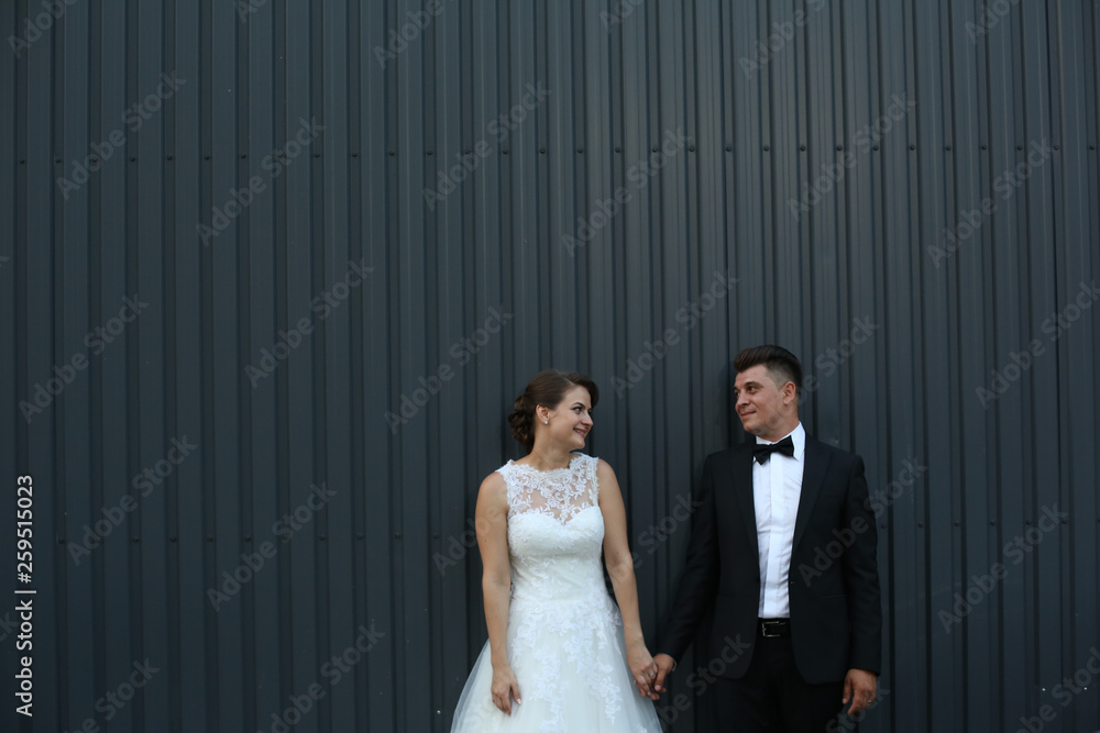 Beautiful wedding couple posing outdoor in front of blue board wall Beautiful wedding couple posing outdoor in front of blue board wall