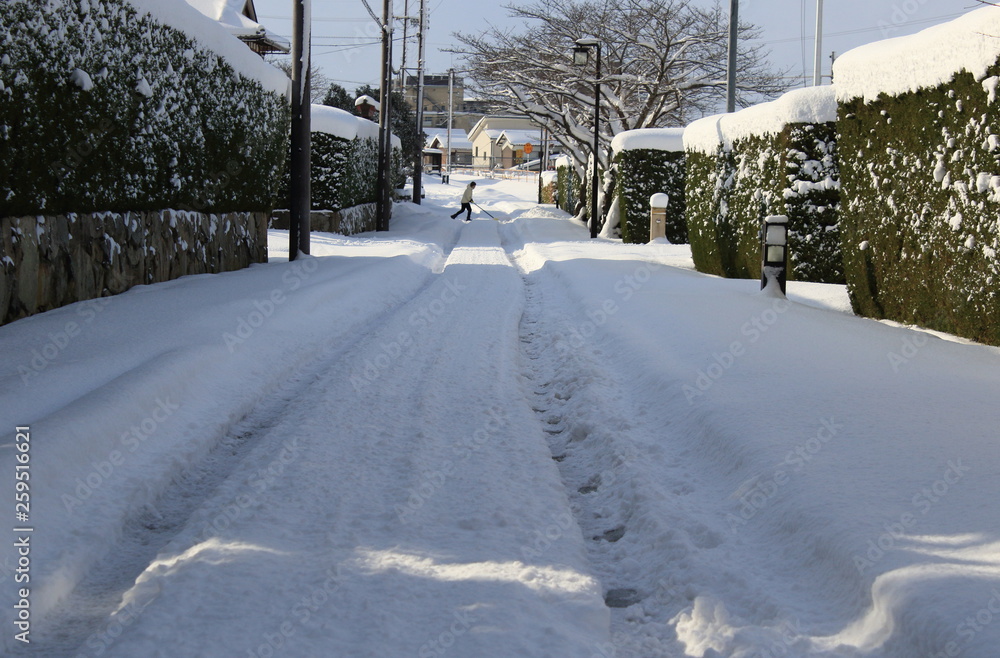 積雪した道路を雪カキをして横切る人の姿
