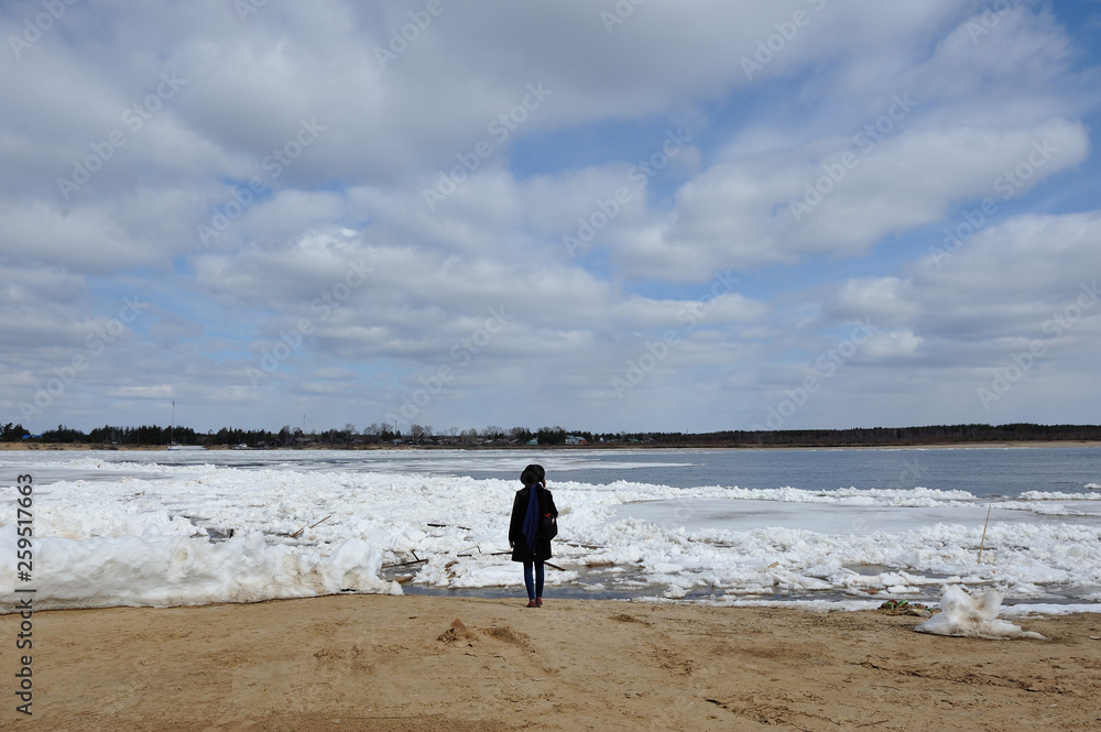 The figure of a girl in a hat, standing on the bank of Vychegda river during the ice drift and admiring.