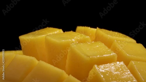 Macro shooting of a mango rotating on the turntable. Juicy sliced, hedgehog style served mango, isolated on the black background