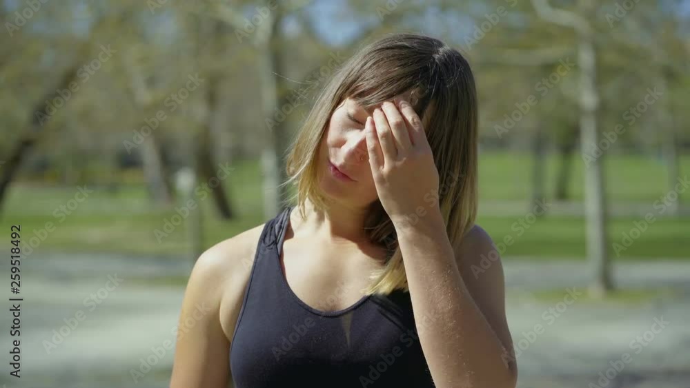Tired young woman drinking water after training in park. Sweaty sportswoman with piercing standing in park during sunny day. Concept of sport Tired young woman drinking water after training in park. Sweaty sportswoman with piercing standing in park during sunny day. Concept of sport