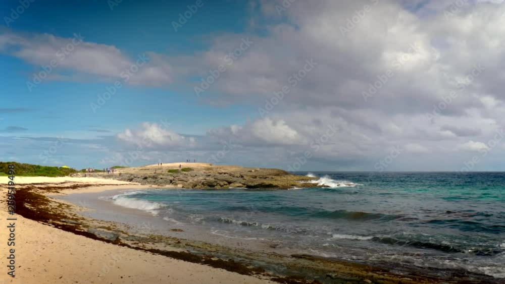 Calm ocean waters roll onto a secluded sandy beach as a person walks alone in the distance Calm ocean waters roll onto a secluded sandy beach as a person walks alone in the distance