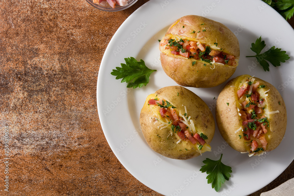 Stuffed potatoes with bacon and cheese on plate on rusty background. Top view