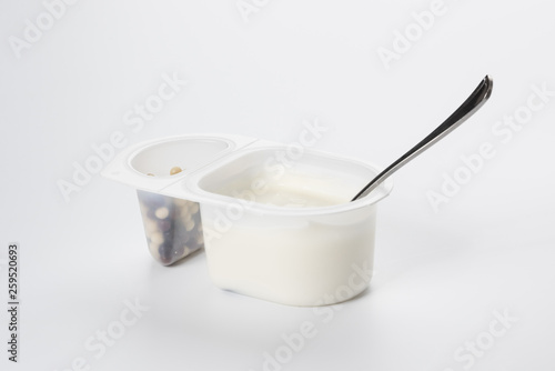 Yogurt with chocolate balls. Double plastic cup with white yogurt and a metal spoon.