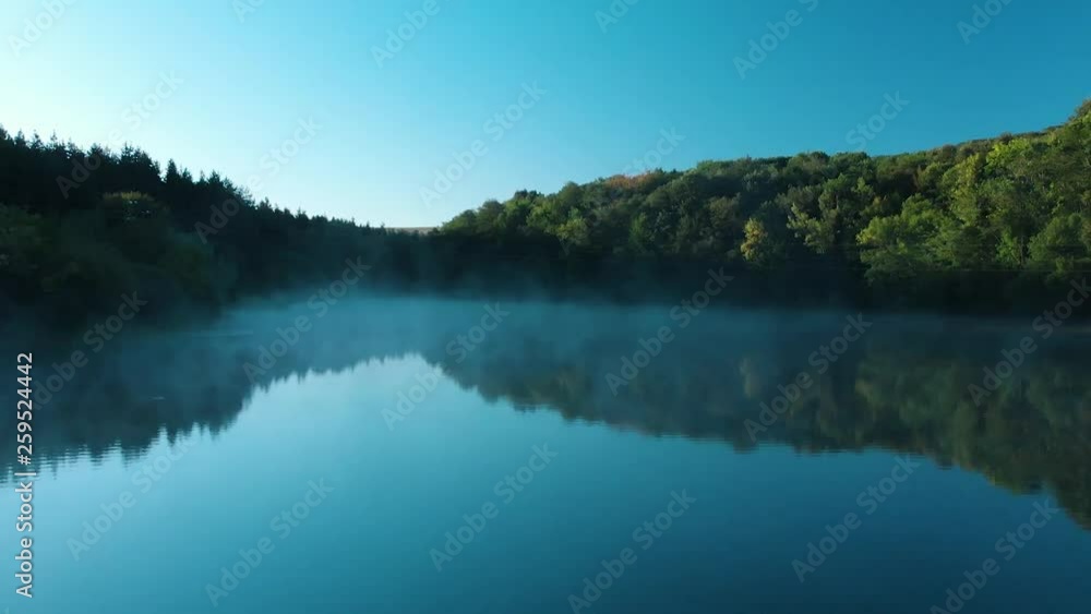 Early morning low drone shot over glossy lake with some fog Early morning low drone shot over glossy lake with some fog
