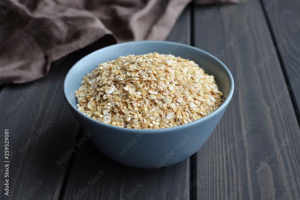 Rolled oats in ceramic bowl on dark wooden table with texture Rolled oats in ceramic bowl on dark wooden table with texture
