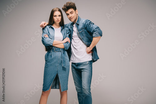 attractive girlfriend in denim dress and boyfriend in jeans and shirt hugging and looking at camera