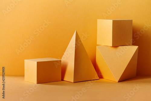 Yellow geometrical figures still life composition. Three-dimensional prism pyramid rectangular cube objects on yellow background. Platonic solids figures, simplicity concept photo