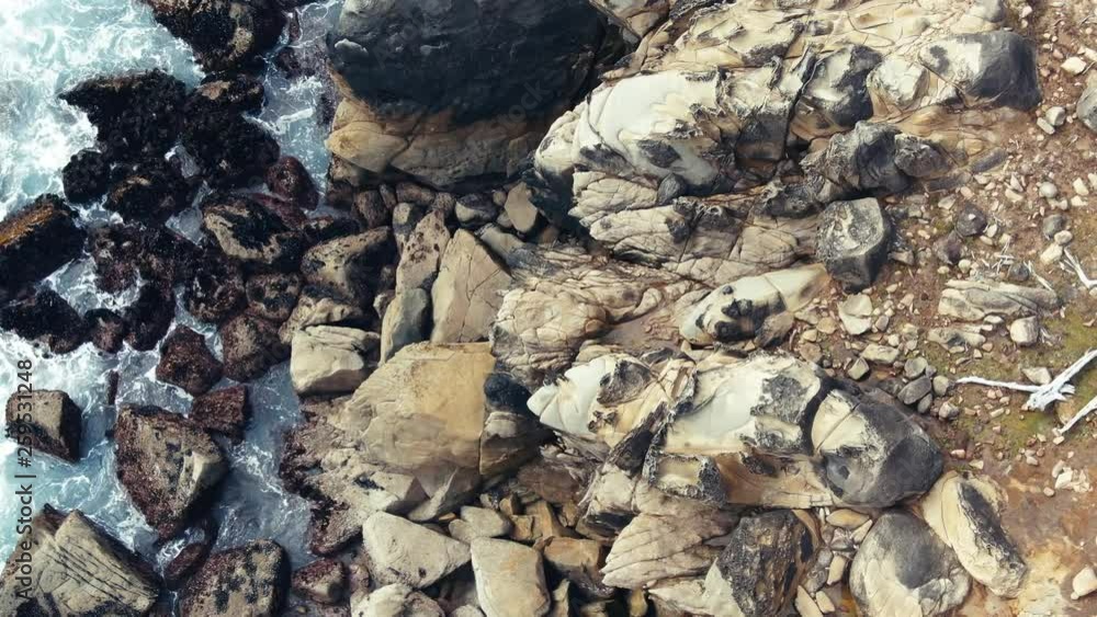 zoom on weather blackened jagged cut orange sandstone cliff overhangs deep teal ocean Drone zoom on weather blackened jagged cut orange sandstone cliff overhangs deep teal ocean Drone