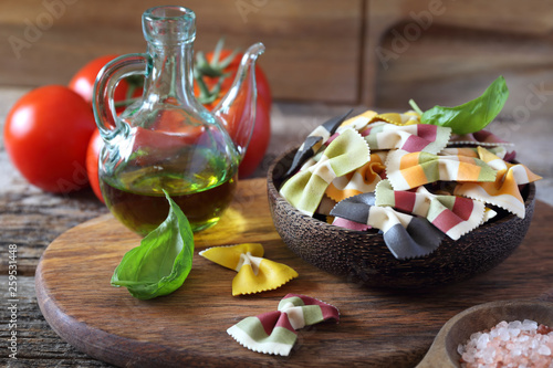 Ingredients of Italian cuisine: raw farfalle pasta, bunch of ripe tomatoes, basil and olive oil