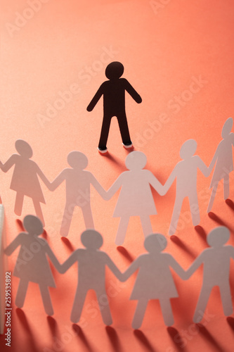 Paper human figure standing in front of paper people holding hands on red surface. Bulling, segregation, conflict concept.