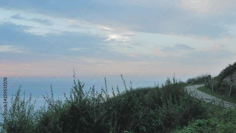 A quiet relaxing scenery: a road in the green countryside, facing a calm blue sea, a cloudy sky; everything is tinted blue and green. A quiet relaxing scenery: a road in the green countryside, facing a calm blue sea, a cloudy sky; everything is tinted blue and green.