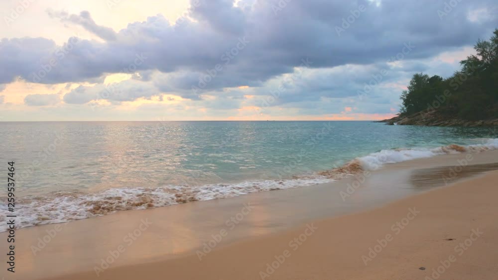 Angled dreamy twilight view of pastel color ocean rippling against the beige sand shore on a cloudy day, sun coming through clouds and creating multicolor glimmer on the surface of the water Angled dreamy twilight view of pastel color ocean rippling against the beige sand shore on a cloudy day, sun coming through clouds and creating multicolor glimmer on the surface of the water