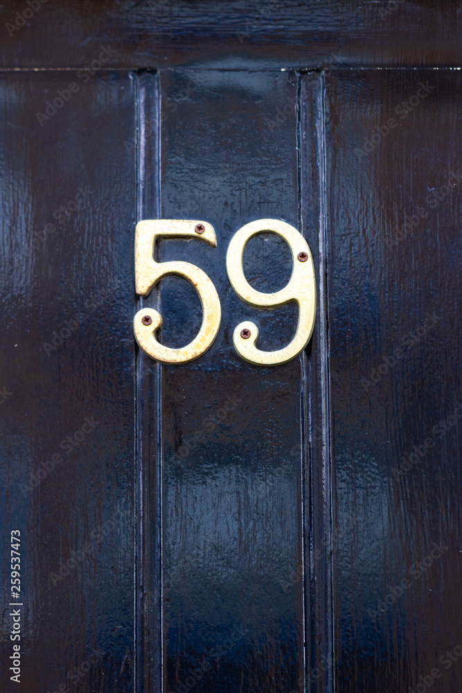 House number 59 with the fifty-nine in curled bronze metal numerals on a black house door carved like planks House number 59 with the fifty-nine in curled bronze metal numerals on a black house door carved like planks