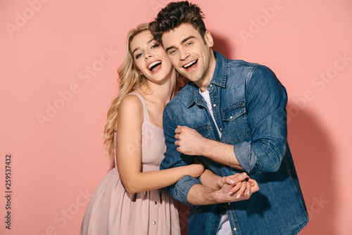 smiling girlfriend in pink dress and handsome boyfriend in denim shirt hugging