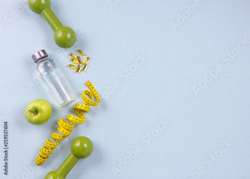 Flat lay bottle of water, measuring tape and fresh green apple on the blue background. Weight loss concept. Top view, copy space.