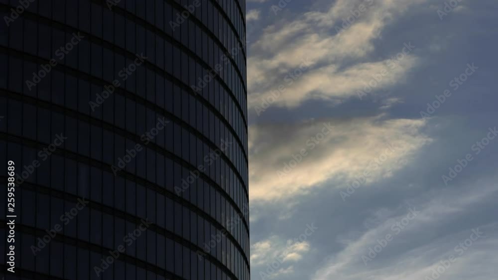 Timelapse with evening clouds flying past steel and glass round-shaped skyscraper corporate office building. Timelapse with evening clouds flying past steel and glass round-shaped skyscraper corporate office building.