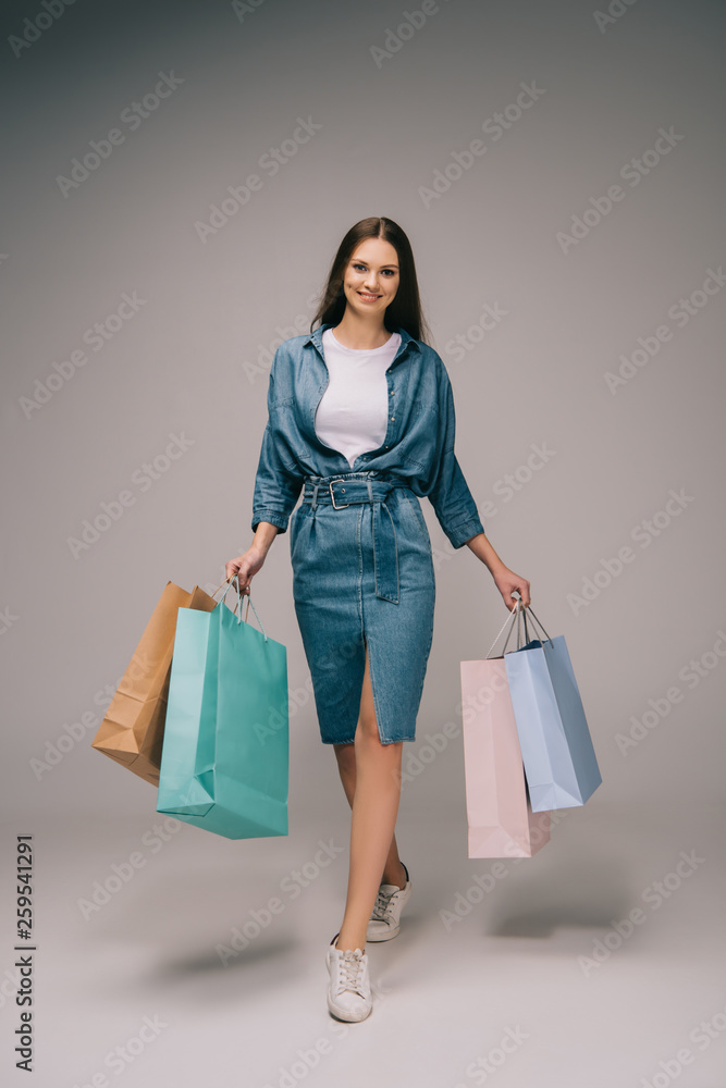 smiling and beautiful woman in denim dress holding shopping bags and looking at camera smiling and beautiful woman in denim dress holding shopping bags and looking at camera