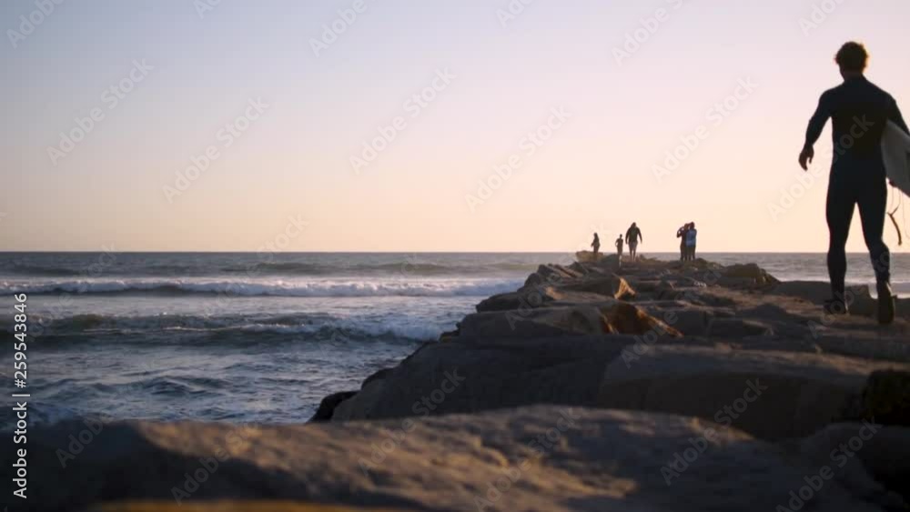 Beautiful, calm and peaceful sunset in San Diego, shooting down a jetty with people and waves crashing alongside it. This shot is in slow motion featuring a surfer running down the jetty. Beautiful, calm and peaceful sunset in San Diego, shooting down a jetty with people and waves crashing alongside it. This shot is in slow motion featuring a surfer running down the jetty.