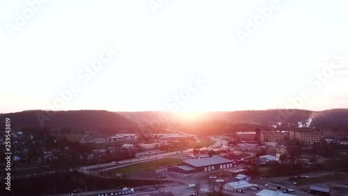 An aerial zoom pan of a beautiful golden sun setting over a small city area with a smoke producing bourbon distillery in the background. photo