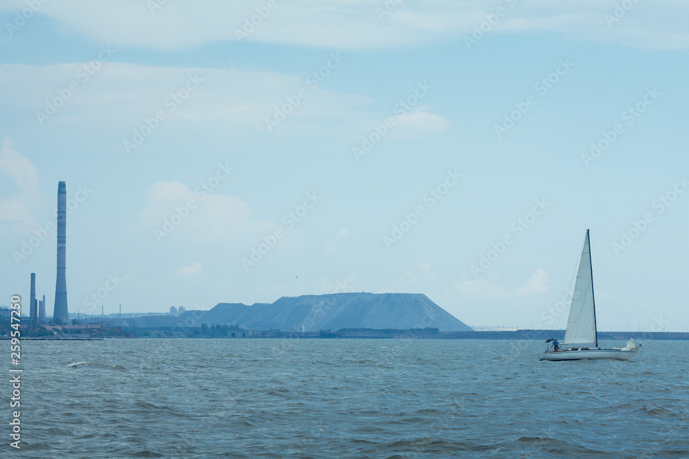 Team of brave men sailing at regatta. Cloudy weather. Industrial landscape on horizon - mountain, city, factory, plant chimney. Outdoor shot