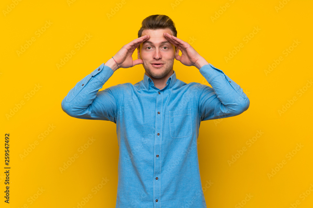 Blonde man over isolated yellow wall with surprise expression Blonde man over isolated yellow wall with surprise expression