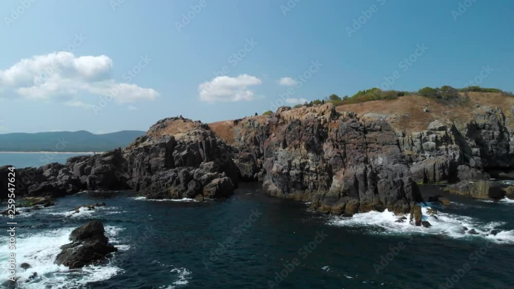 Aerial pan shot of big rocks in the sea next to the shore in sunny summer
day Aerial pan shot of big rocks in the sea next to the shore in sunny summer
day