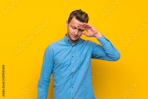 Blonde man over isolated yellow wall with tired and sick expression