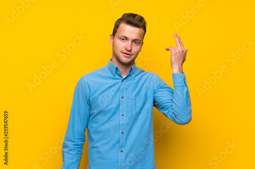 Blonde man over isolated yellow wall with problems making suicide gesture