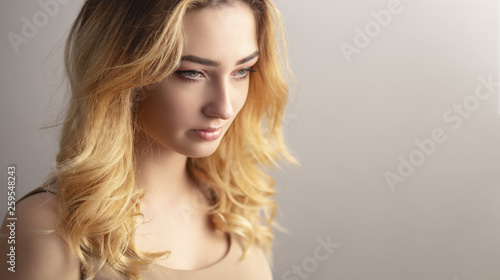 soft studio portrait of a confident young woman, girl face with curly hair disheveled from wind , the concept of natural beauty, body care, cosmetics