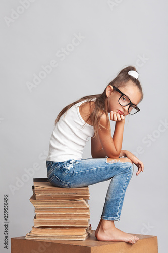 Hard teaching, learning, educational, self-educational process concept. Portrait of funny tired girl sitting on a bale of papers over light gray background. Copy-space. Studio shot