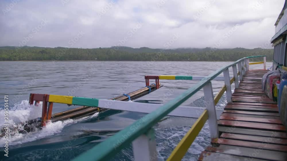 Wooden outrigger slices through the water creating small waves as a boat motors toward land. Wooden deck of a ferry approaching an island in the Philippines. Slow motion. Wooden outrigger slices through the water creating small waves as a boat motors toward land. Wooden deck of a ferry approaching an island in the Philippines. Slow motion.