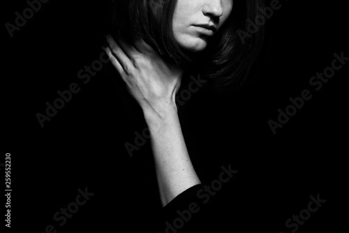  metoo movement concept. Closeup portrait of young woman hiding face  posing with hand on neck  isolated on black background. Human emotion  expression  rights   communication. Text space. Monochrome